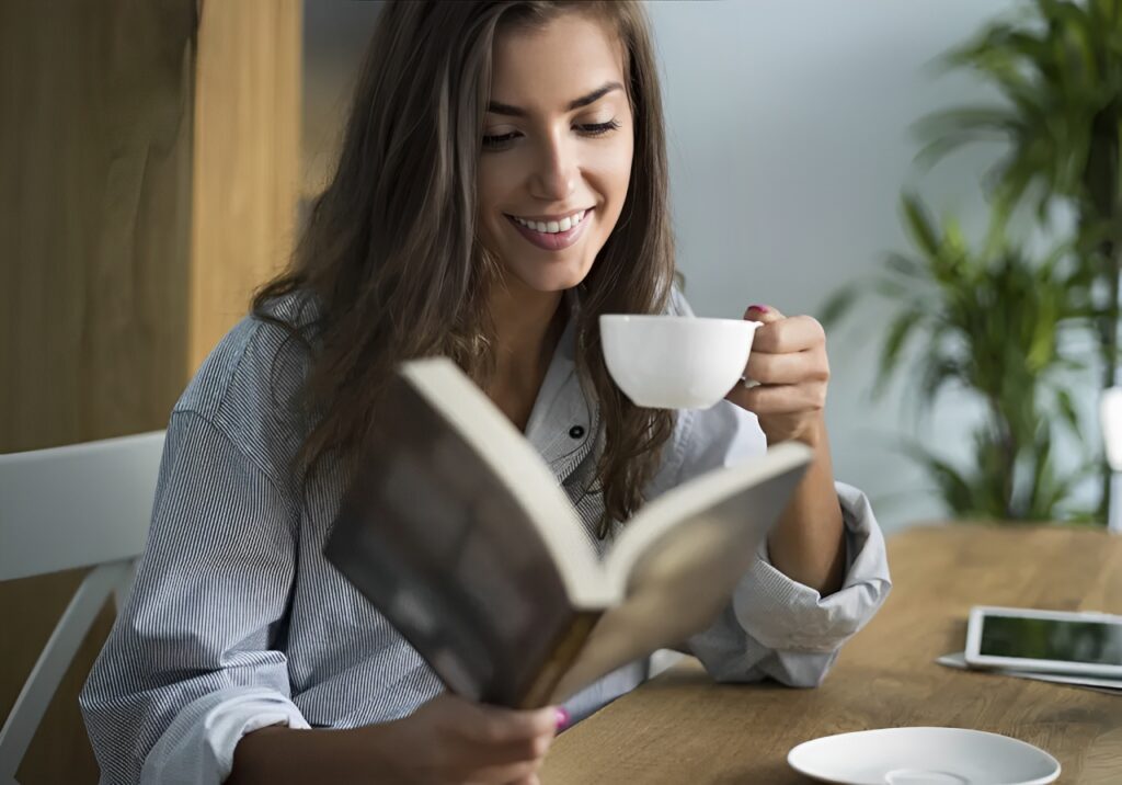 A woman is drinking coffee and reading a book.